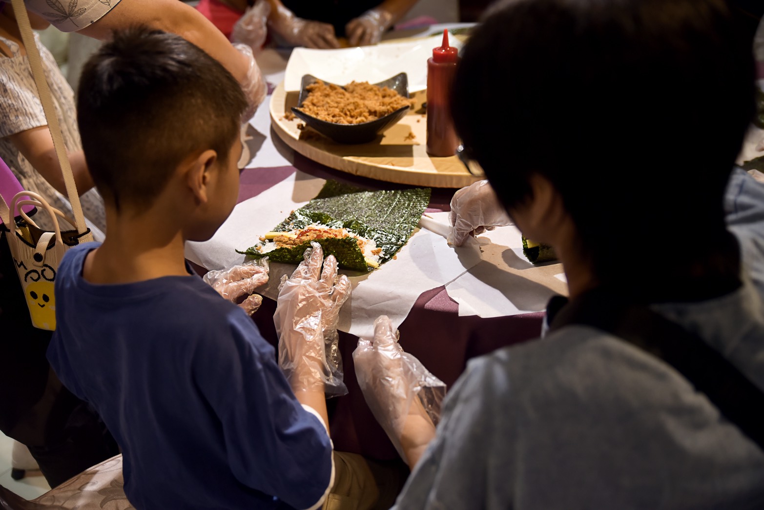 孩子在家長與工作人員陪伴下體驗手作壽司，從鋪飯、放置食材到捲製餐點，享受動手做的樂趣。（圖／主辦單位提供）