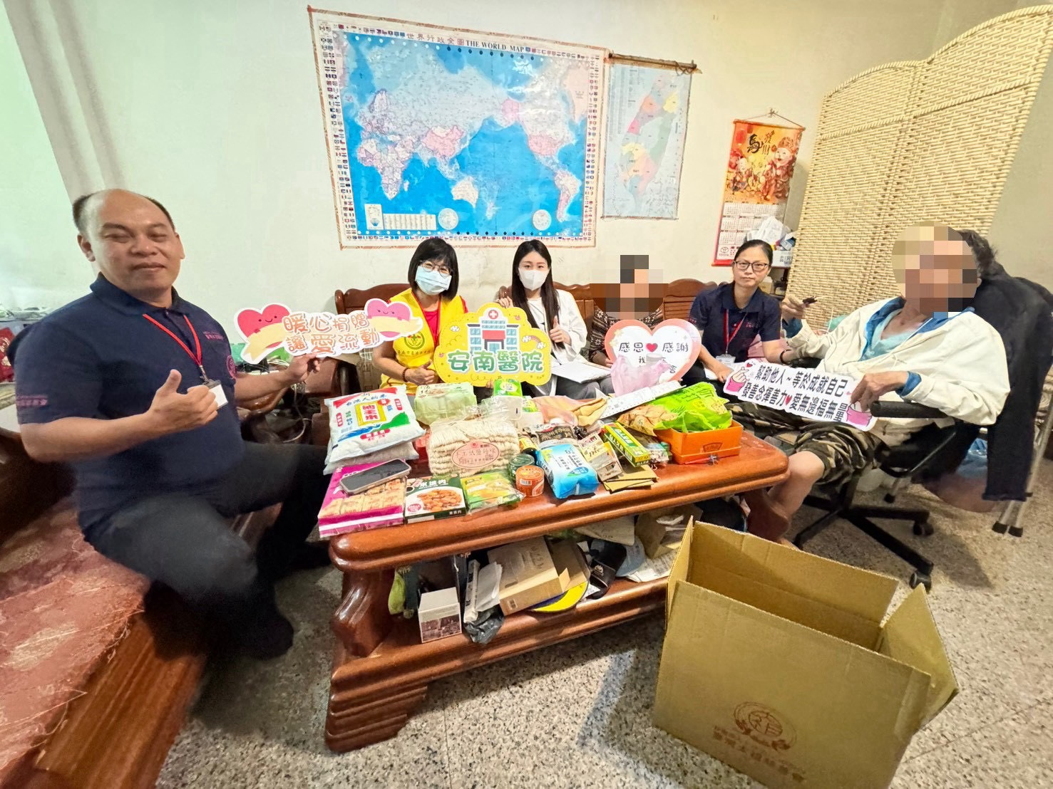 訪視人員與家庭成員在室內合影,桌上擺放民生物資,部分臉部已有馬賽克遮蔽